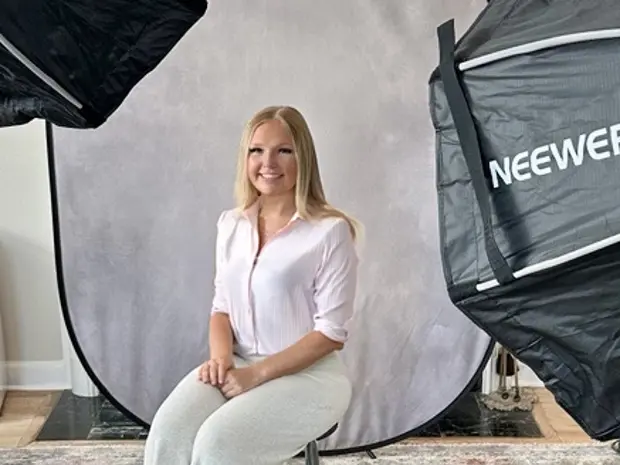 Female subject sitting and posing for a photo with a gray backdrop and lighting umbrellas around. 
