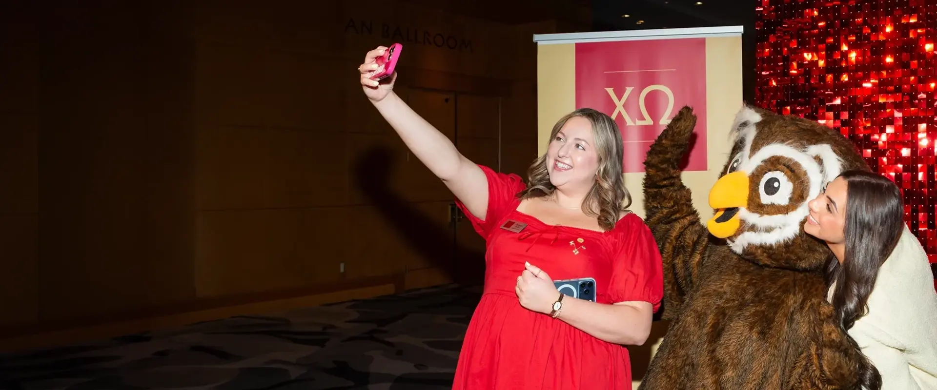Girls taking a selfie with an owl mascot at a Chi Omega sorority convention. 