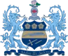 Alpha Xi Delta sorority crest featuring a navy and gold shield with three roses, a quill, and crossed sword and pen, flanked by two blue griffin supporters, topped by a knight's helmet and pink rose, with a navy banner