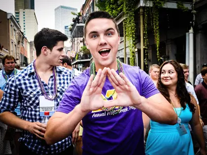Fraternity member in a parade making a delta symbol with his hands on the streets of New Orleans. 
