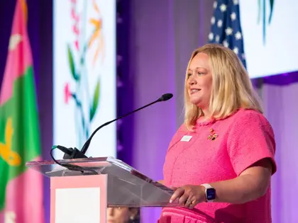 Woman in a pink dress standing at a podium giving a speech or award. 