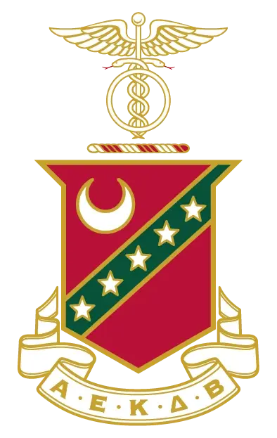 Kappa Sigma fraternity crest featuring a crimson and green shield with a crescent moon, four stars, and a diagonal stripe, topped by a caduceus symbol, with a white banner reading "Α Ε Κ Δ Β."