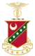 Kappa Sigma fraternity crest featuring a crimson and green shield with a crescent moon, four stars, and a diagonal stripe, topped by a caduceus symbol, with a white banner reading "Α Ε Κ Δ Β."