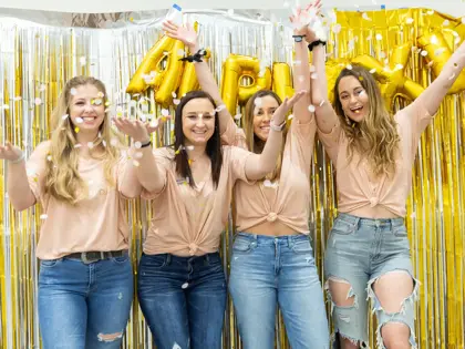 Group of sorority girls wearing feather boas throwing confetti. 