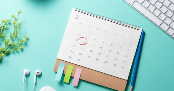A desk calendar with a date circled in red, surrounded by earbuds and sticky notes, representing scheduling composite photo sessions.