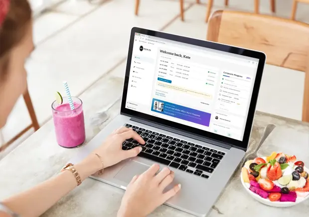 Girl at a cafe with a smoothie and fruit bowl on a table alongside a laptop with a website open. 